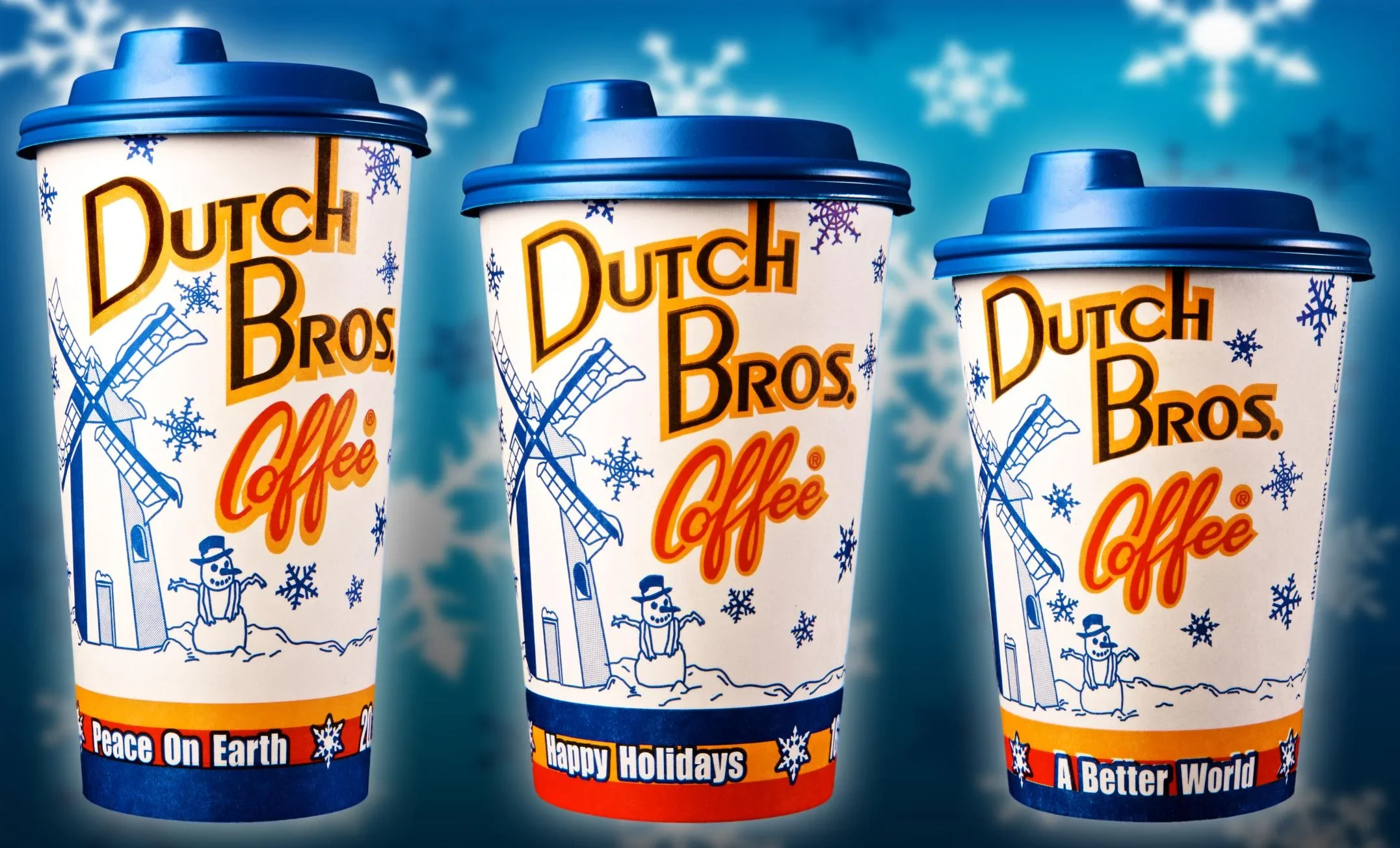 Three Dutch Bros Coffee holiday cups with blue lids featuring winter designs and different seasonal messages.