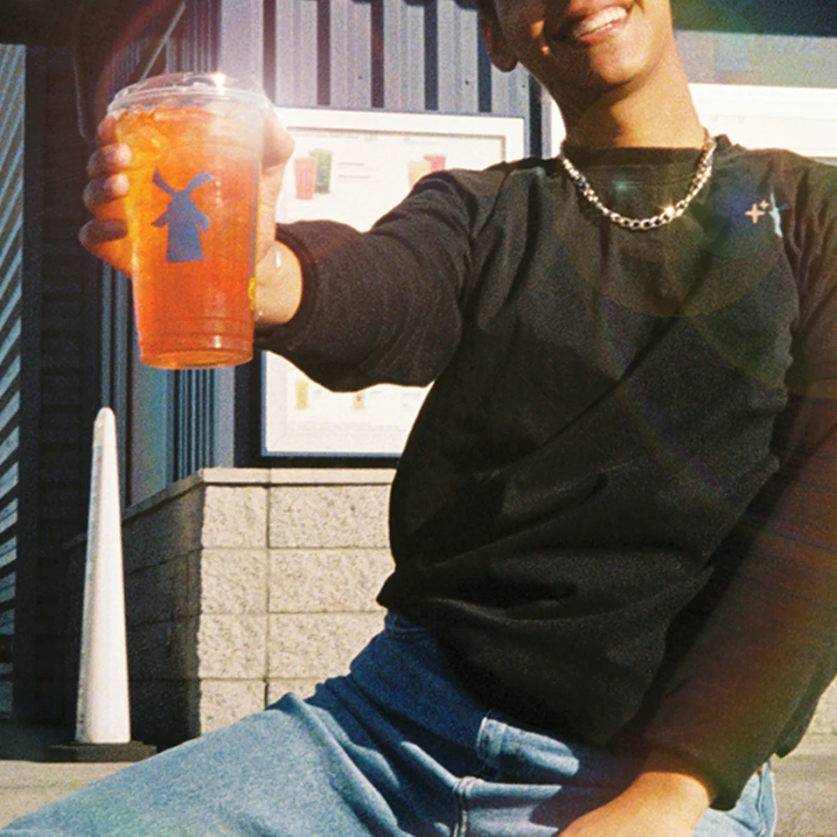 Person in black sweater holding an orange Dutch Bros drink cup with blue windmill logo outside a building.