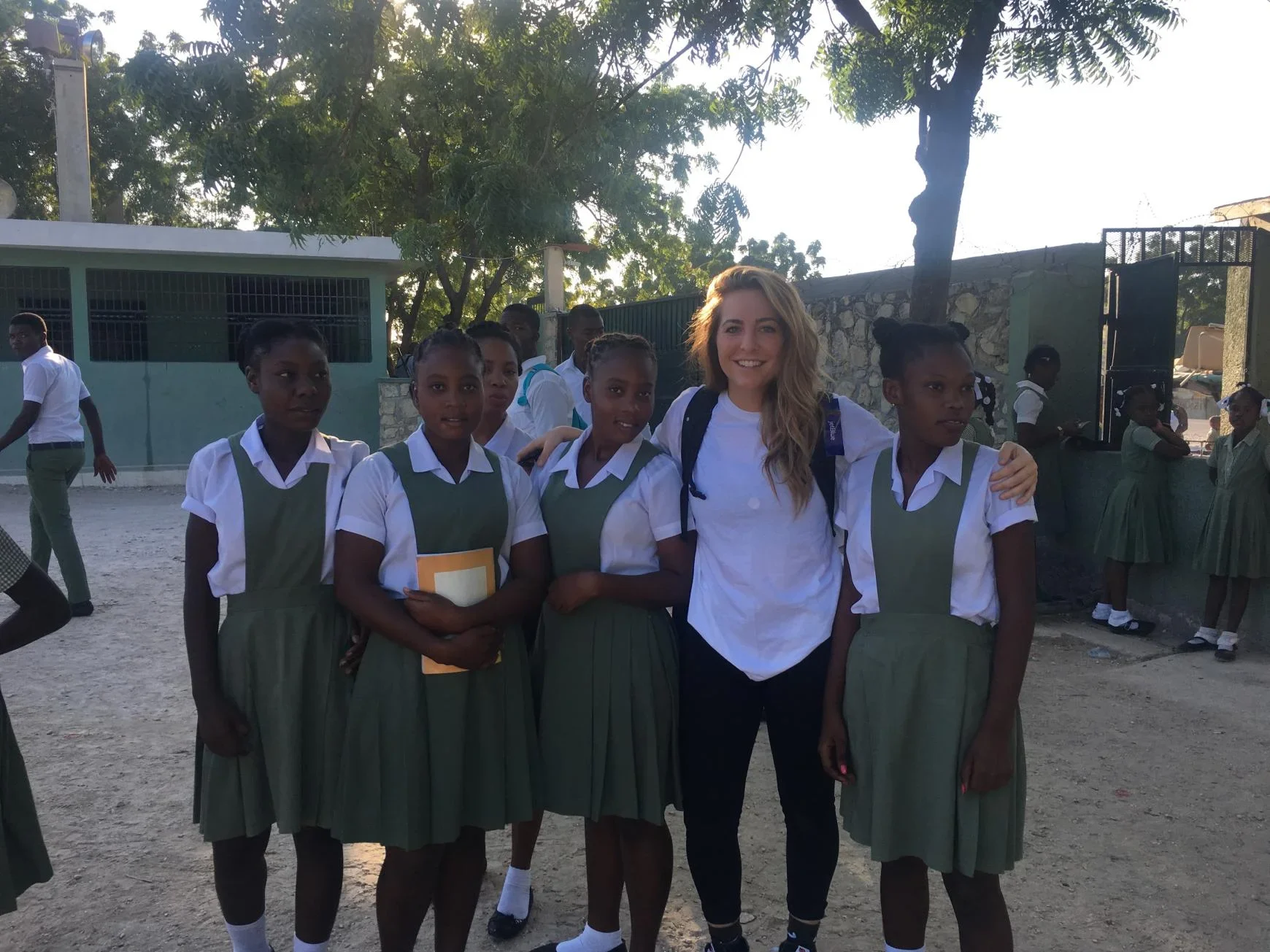 Group of students in green uniforms with white shirts posing together at a school compound with trees in background.