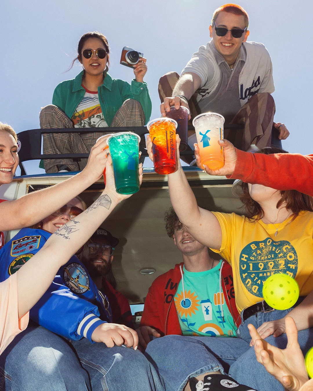 Young people in a vehicle toasting with colorful drinks while enjoying a sunny day together outdoors.