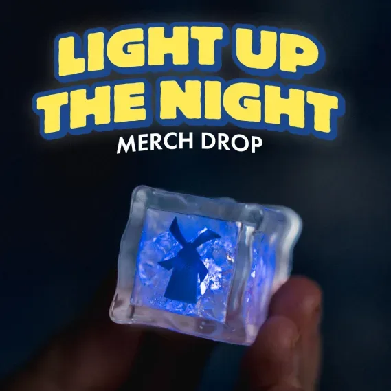 A hand holds a glowing blue translucent keycap with a dark logo. Text reads "Light Up the Night Merch Drop."