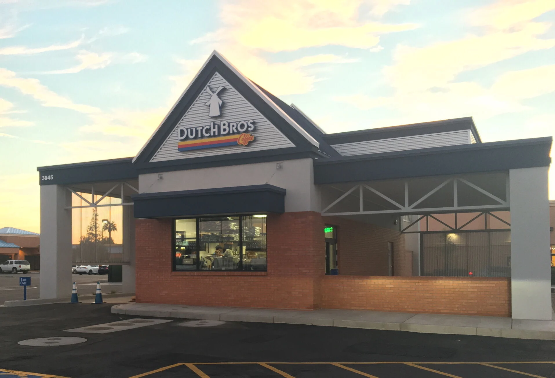 Dutch Bros Coffee shop exterior with distinctive triangular roof sign, brick base, and drive-thru lane at sunset.