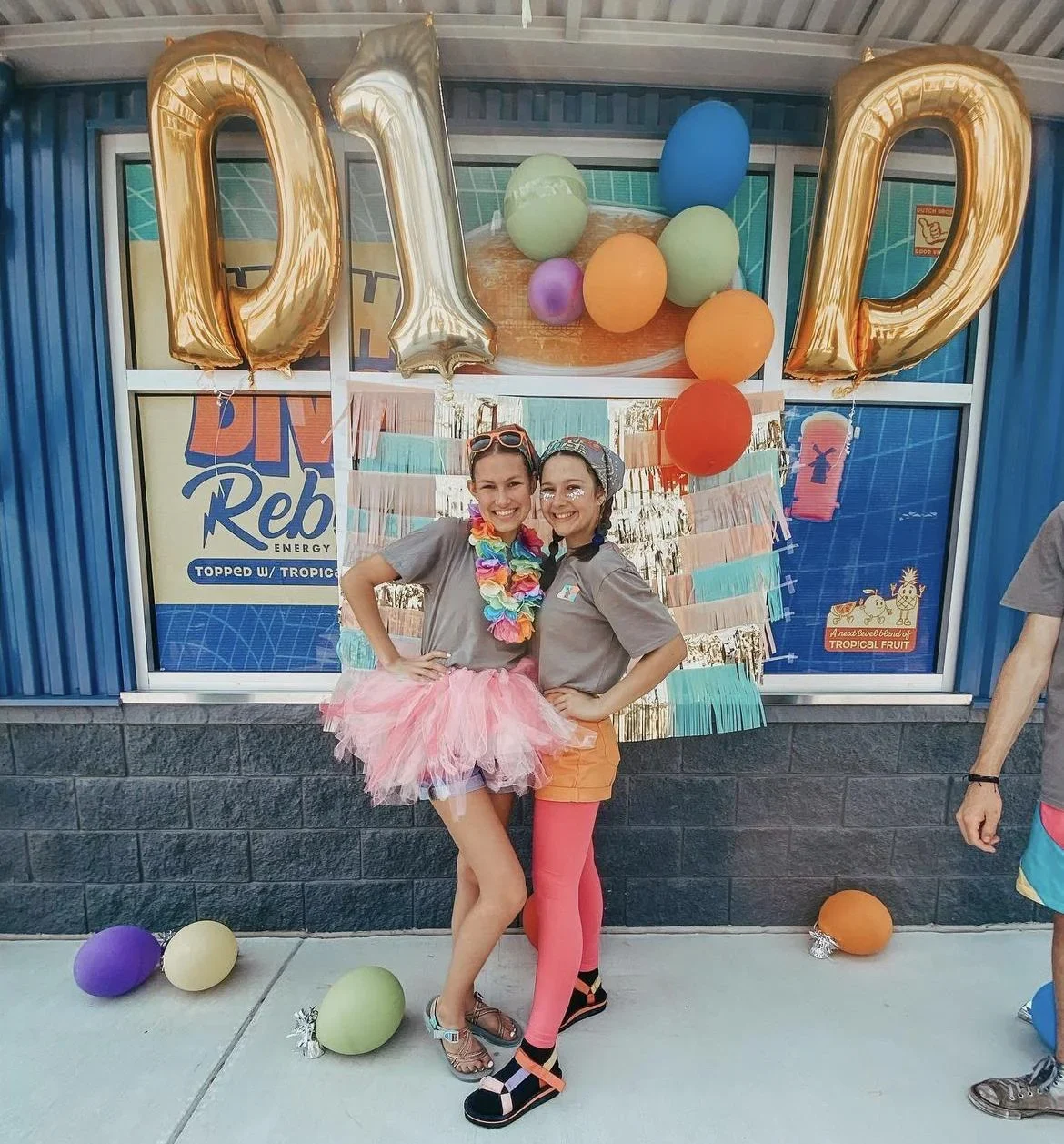 Festive tropical party with gold "DAD" balloons, colorful decorations, and two people in bright costumes with leis.