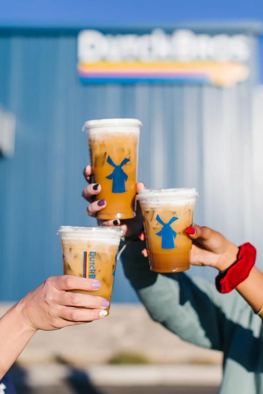 Three hands holding iced coffee drinks in plastic cups with blue windmill logos from Dutch Bros Coffee.