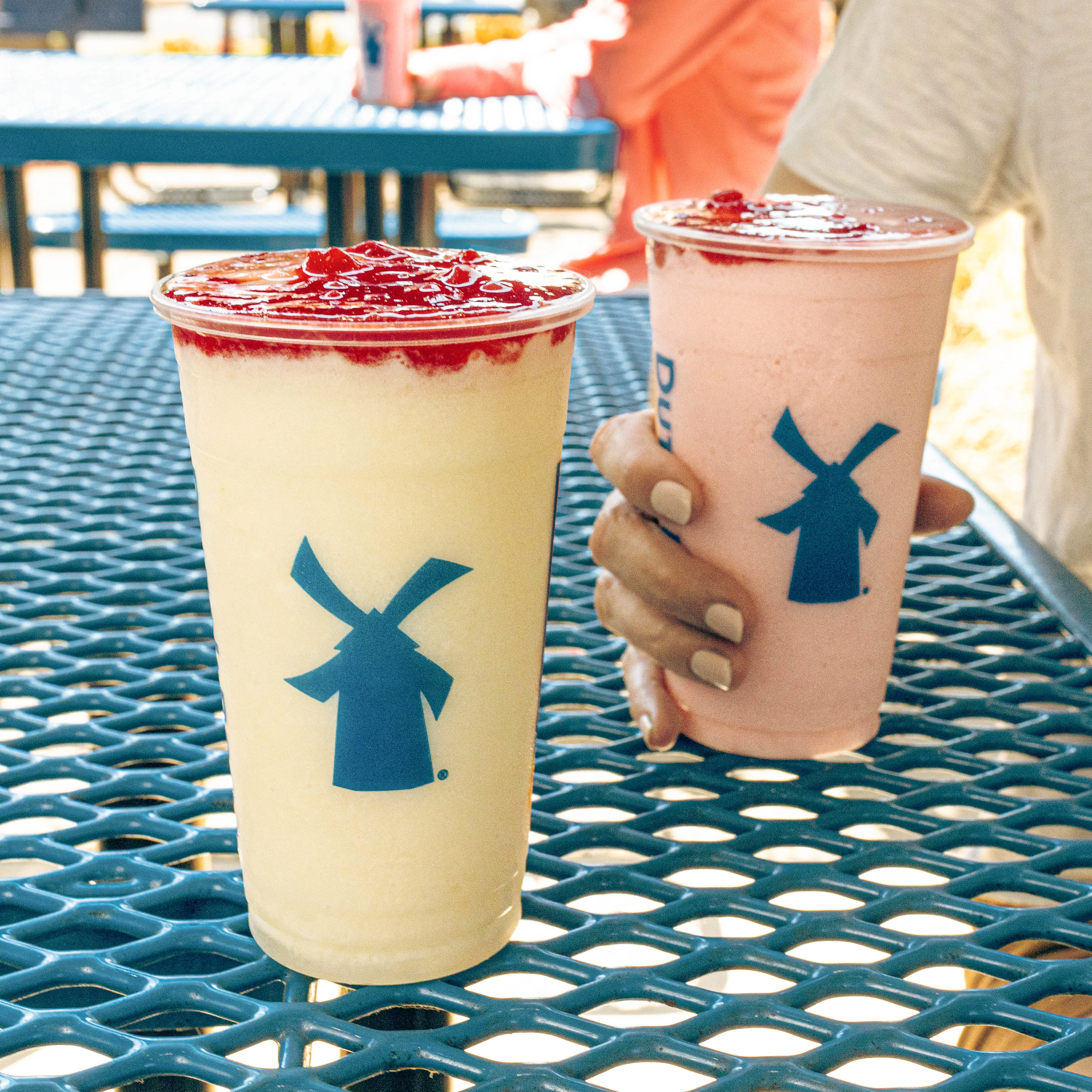 Two Dutch Bros drinks with blue windmill logos and red berry topping on a blue metal patio table.