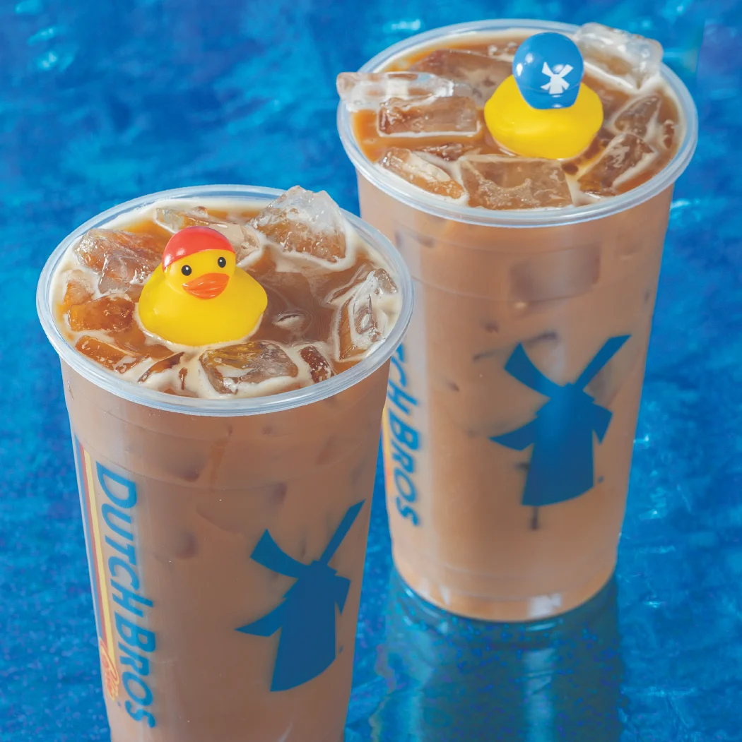Two iced coffee drinks from Dutch Bros with rubber ducks on top against a blue background.