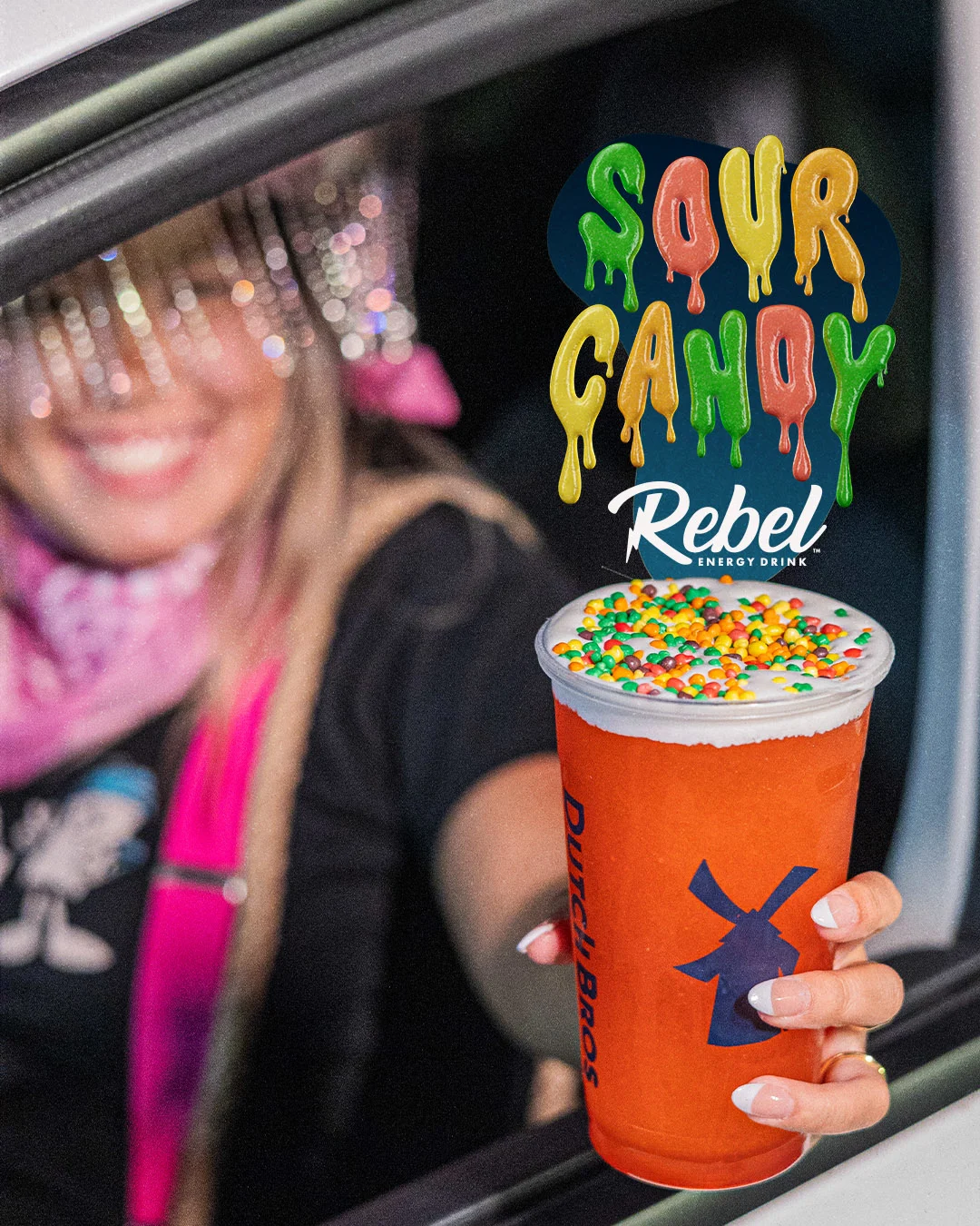 Orange Sour Candy Rebel energy drink topped with colorful candy pieces, held by someone in a car window.