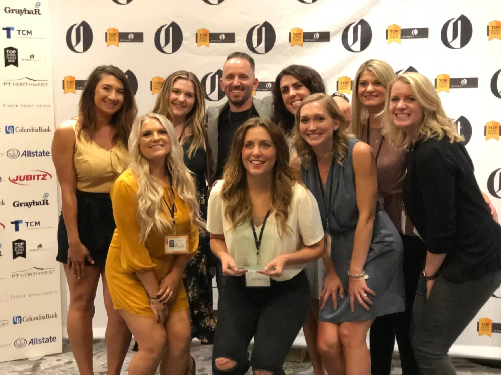 Group posing at an awards event with sponsor backdrop featuring "TOP" banners, one person holding a trophy.