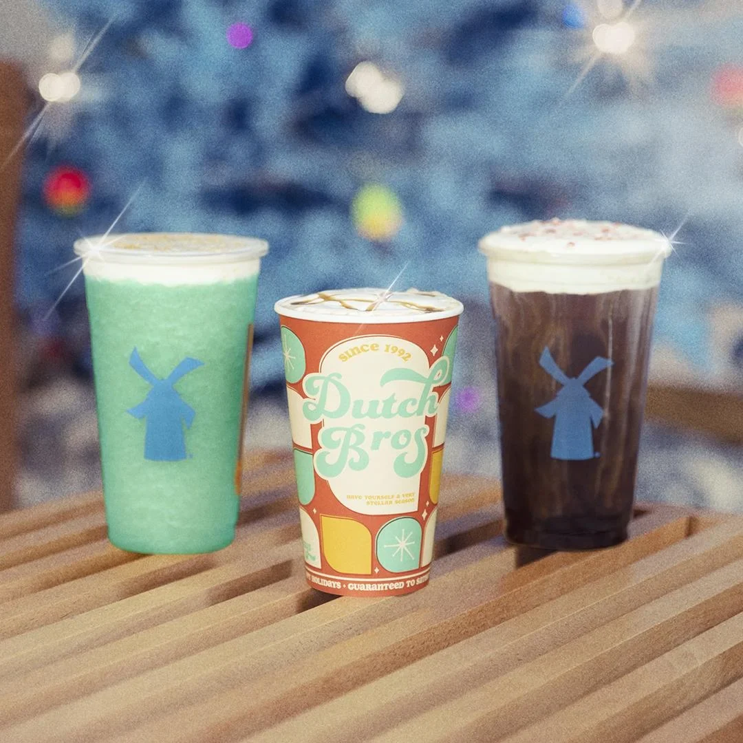 Three Dutch Bros drinks on wooden surface - mint green, branded paper cup, and chocolate beverages with windmill logos.