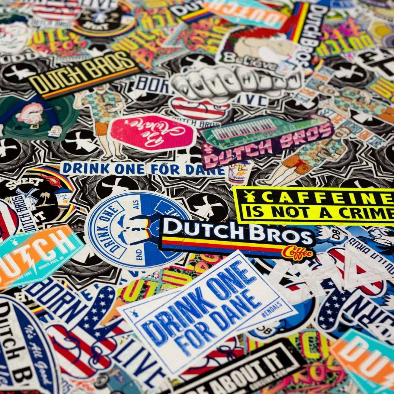 Colorful collection of Dutch Bros coffee stickers featuring slogans like "Caffeine is Not a Crime" and "Drink One For Dane"