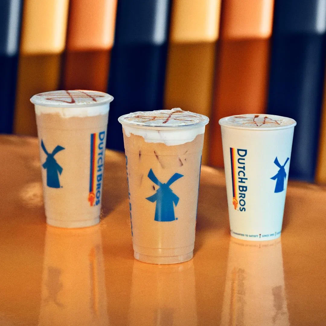 Three Dutch Bros coffee drinks in various sizes with blue windmill logos and caramel drizzle on top.