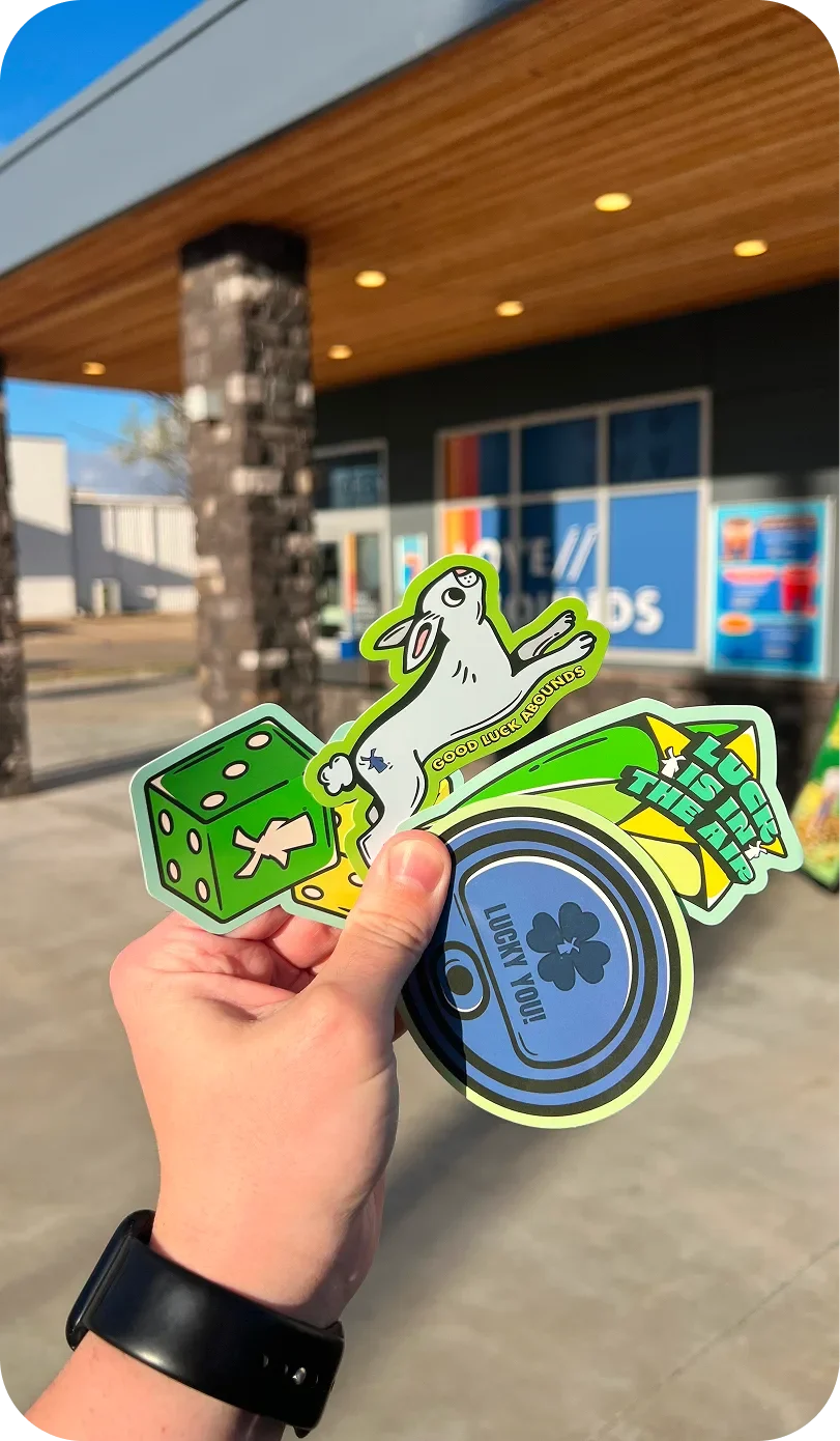 A hand holding luck-themed stickers featuring a rabbit, green dice, and a shamrock coin outside a store.