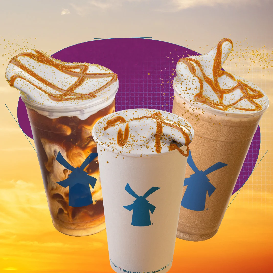 Three Dutch Bros coffee drinks with caramel drizzle and whipped cream against a sunset backdrop with purple circle.