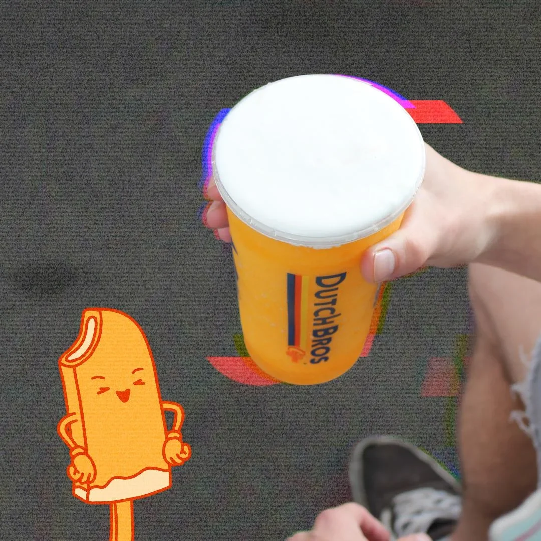 Hand holding a Dutch Bros orange cup with white lid, alongside a cartoon popsicle character with a smiling face.