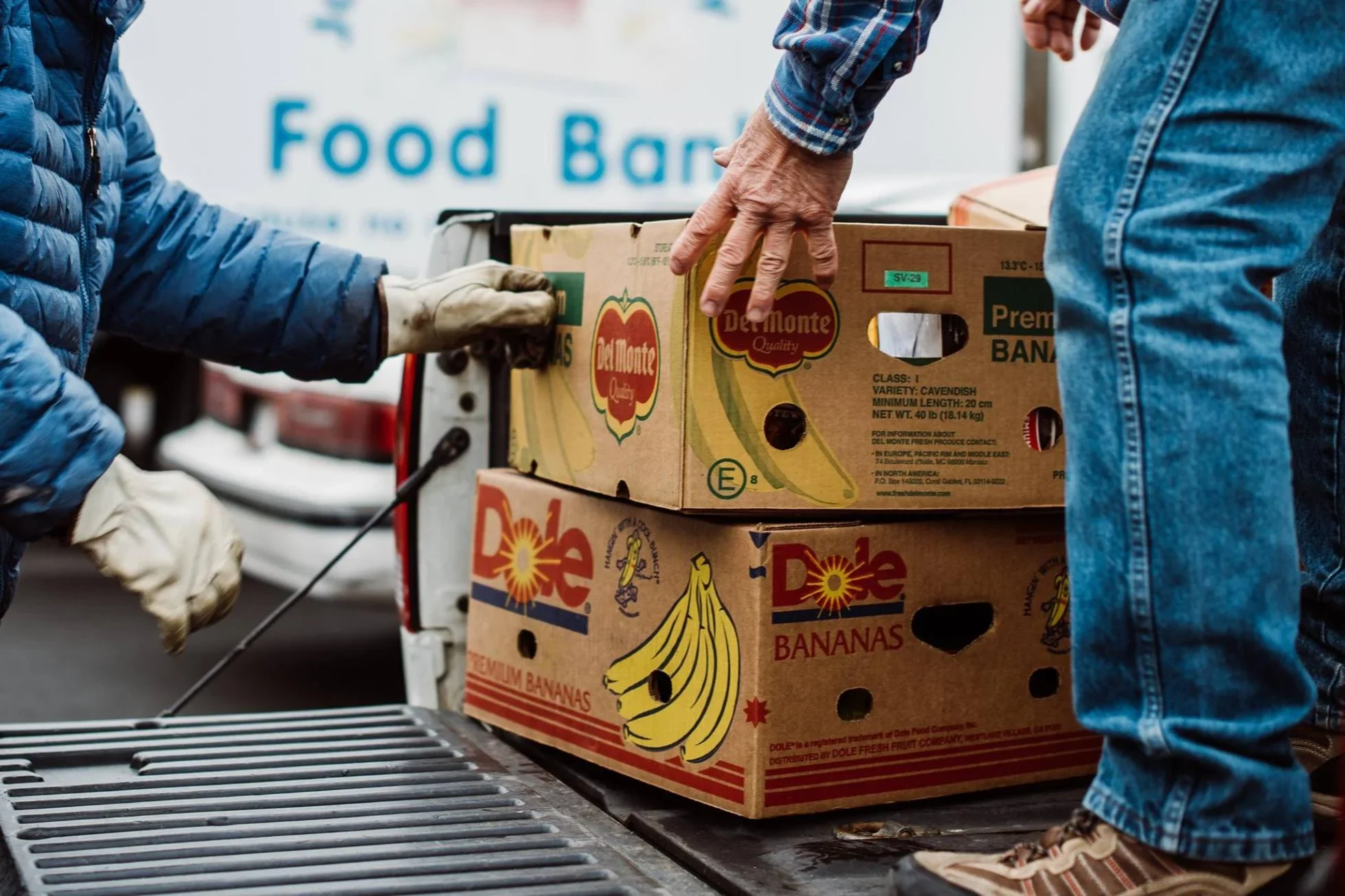 Volunteers unloading boxes of Del Monte and Dole bananas at a food bank, with "Food Ban" visible in the background.
