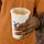 A person's hand holding a hot chai with cinnamon sprinkles