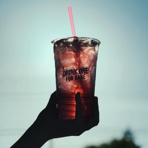A clear Dutch Bros cup is held up in front of the sun for a cool effect