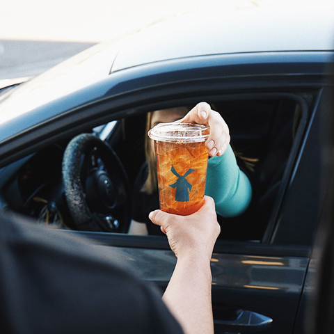 A iced peach tea is handed out the drive through window to a customer in their car