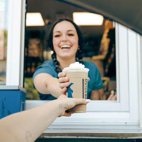 A smiling broista hands a drink out the window