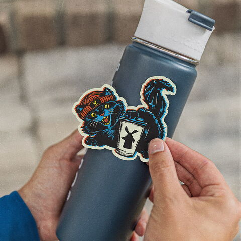 Hands holding a tumbler with a sticker of a cat in front of it 