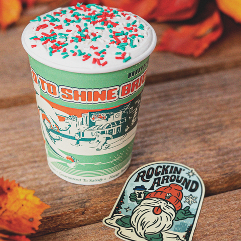 A drink with sprinkles on a table with fall leaves next to the sticker of the month