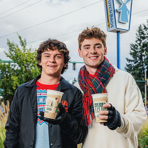 two boys standing infront of the dutch bros sign holding cold dutch bros drinks with Christmas sweaters