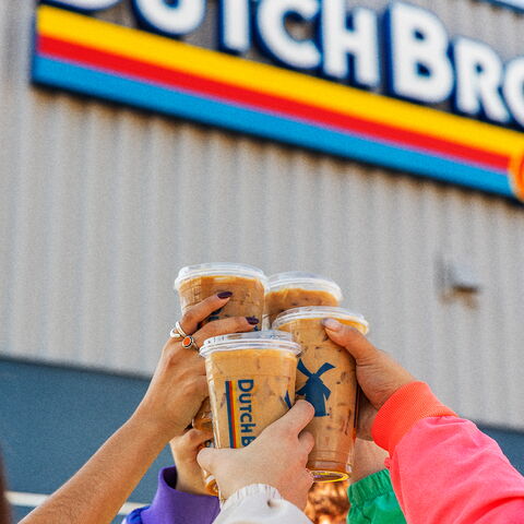 hands cheersing with iced coffees in front of Dutch Bros 