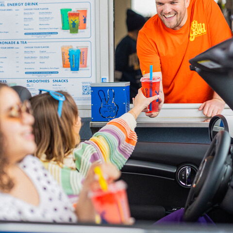 A smiling broista holding a drink out to a customer