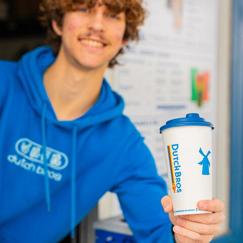 A smiling broista holding a Dutch Bros drink out the window.