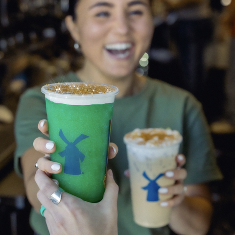 A smiling broista handing two drinks out the window.