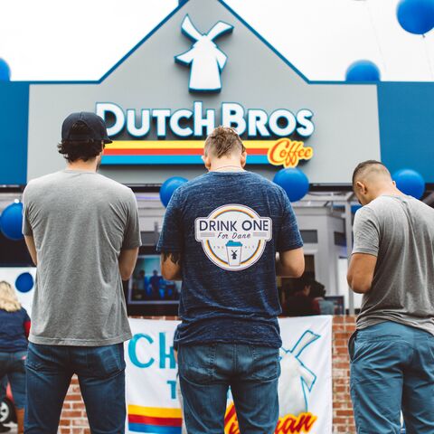 A group is shown bowing their heads in prayer and reflection outside of a Dutch Bros location
