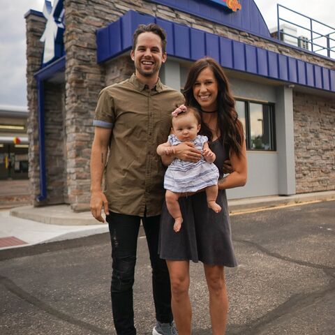 A couple holds their baby and smiles outside of a Dutch Bros location 